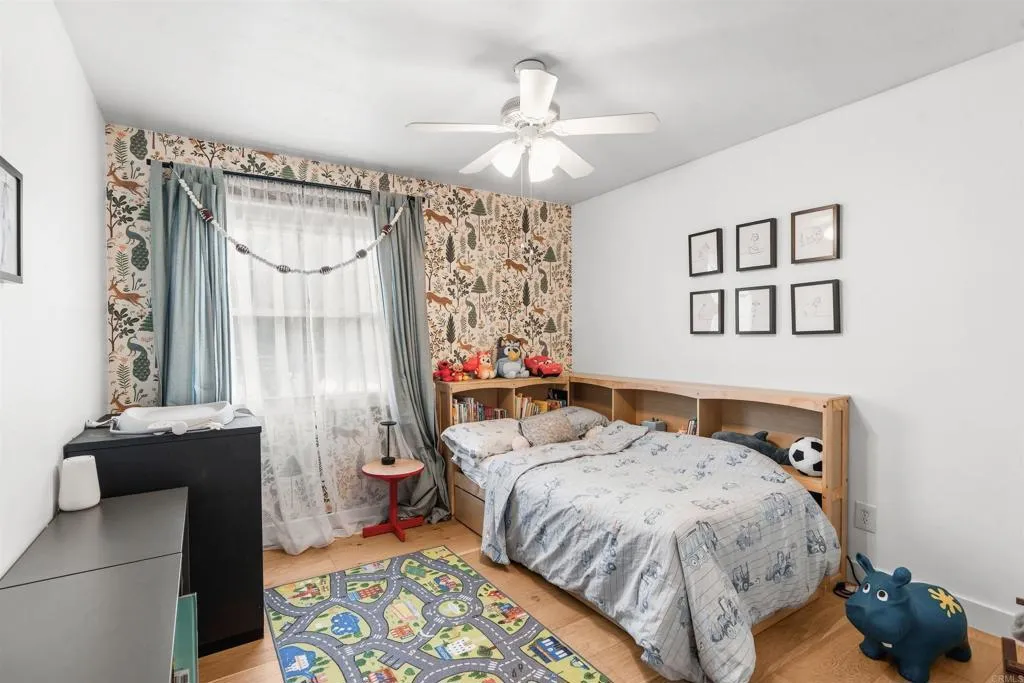 Bedroom with a low wooden bookcase behind the bed and a colorful road-map rug.