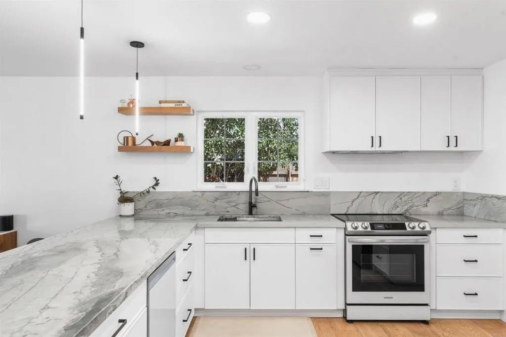 Bright white kitchen with veined stone counters, stainless-steel range, and a window above the sink.