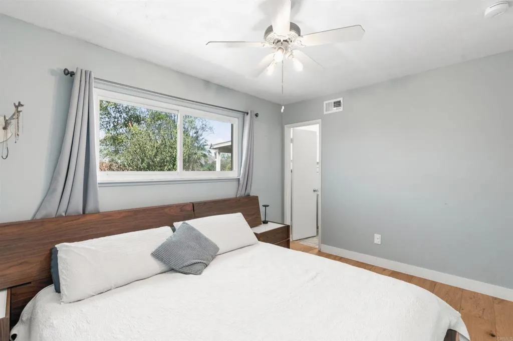 Bedroom with a white bed, dark wood headboard, and a wide window overlooking leafy trees.