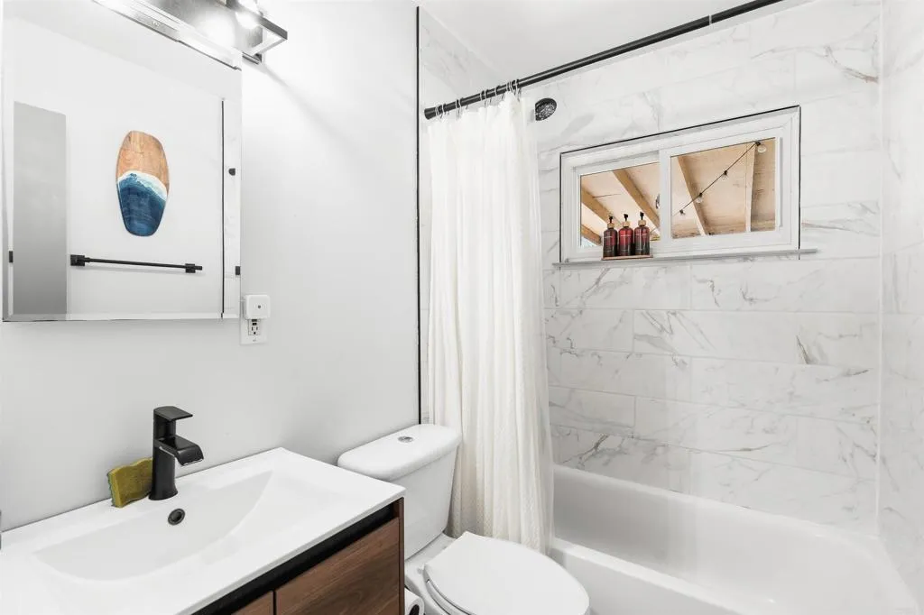 Bathroom with marble-look shower walls, white tub, and wood-front vanity.
