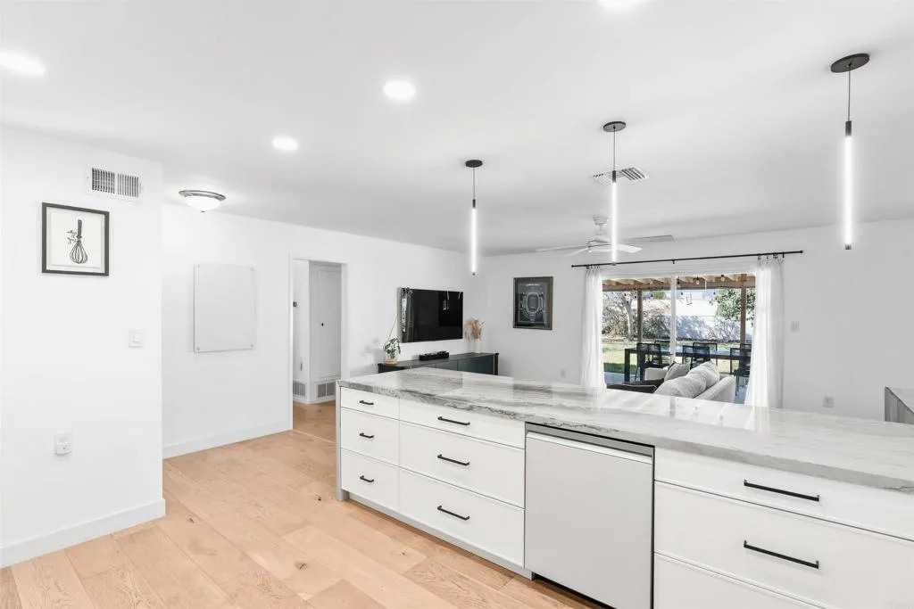Open-plan kitchen with a large marble-look island, white cabinets, and light wood floors.