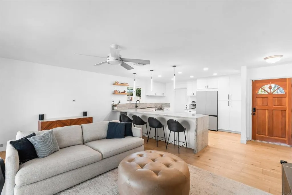 Open-plan living room and kitchen with a gray sofa, marble-look island, and wood front door.
