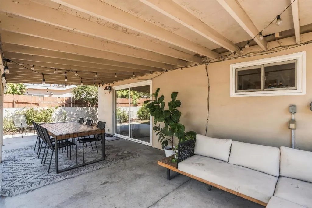 Covered patio with string lights, a dining set on a patterned rug, and a light sofa beside sliding glass doors.