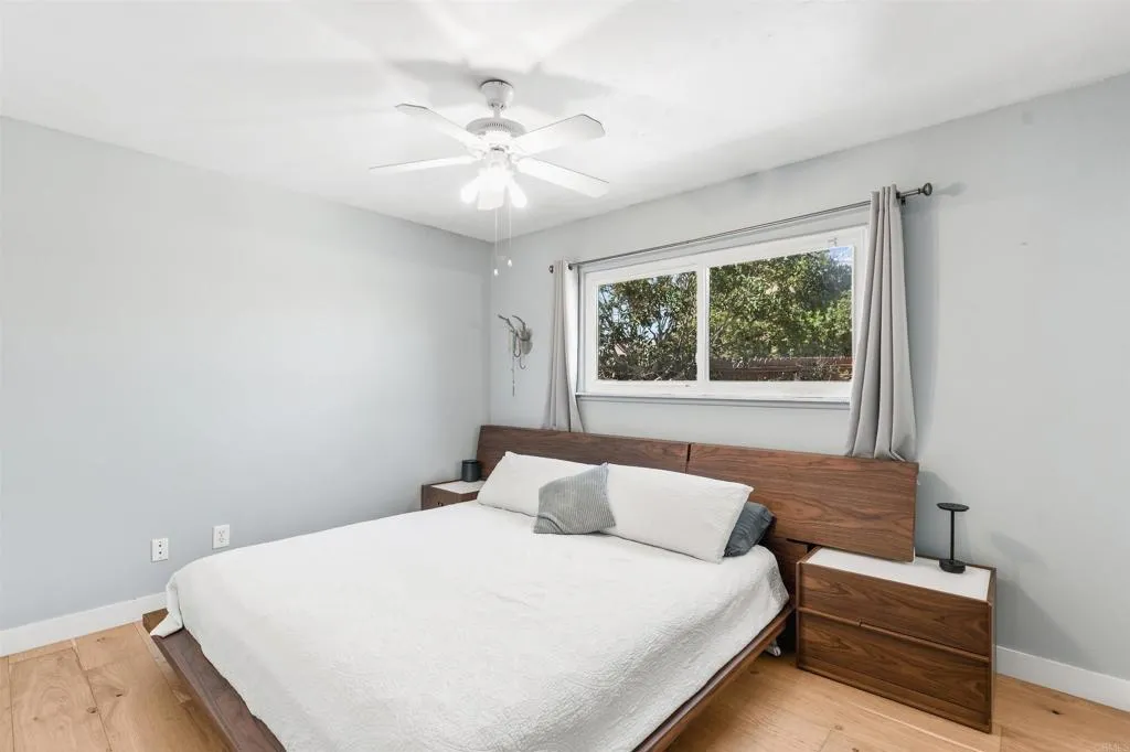 Bedroom with a white bed, wooden headboard, matching nightstands, and a window overlooking trees.