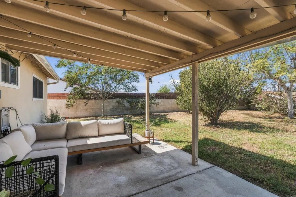 Covered backyard patio with string lights and a gray sectional overlooking a fenced yard.
