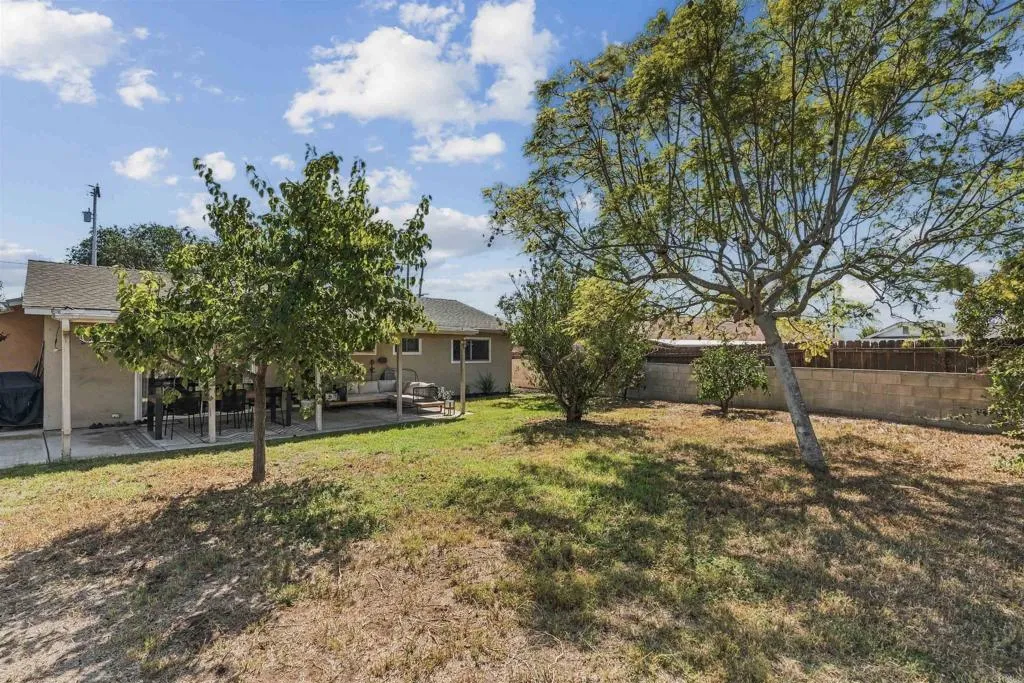 Backyard with a covered patio, outdoor furniture, mature trees, and a dry lawn.