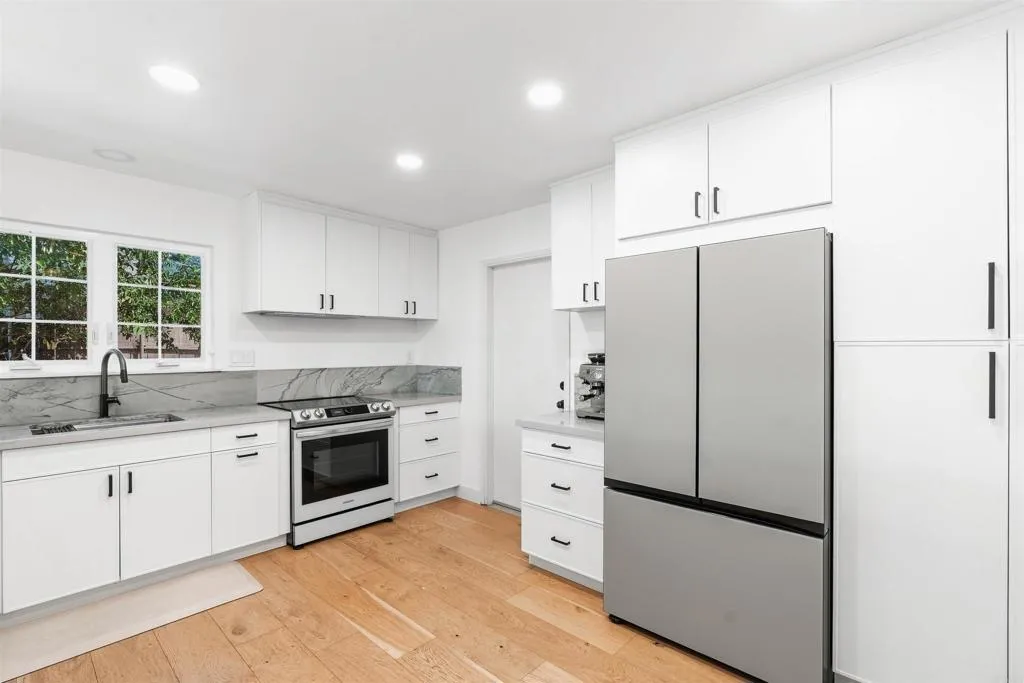 Bright white kitchen with stainless steel appliances, marble-look counters, and light wood flooring.
