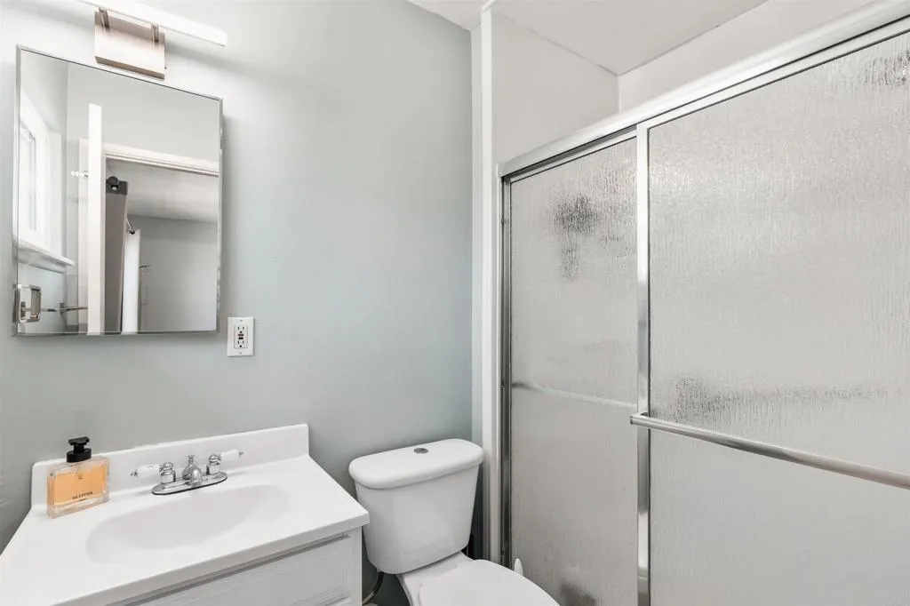 Bathroom with a white vanity, toilet, and frosted-glass sliding shower door.