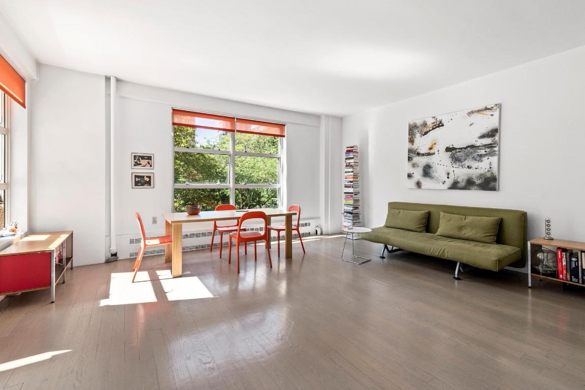Living and dining area with large windows, red-orange chairs, and a green sofa.