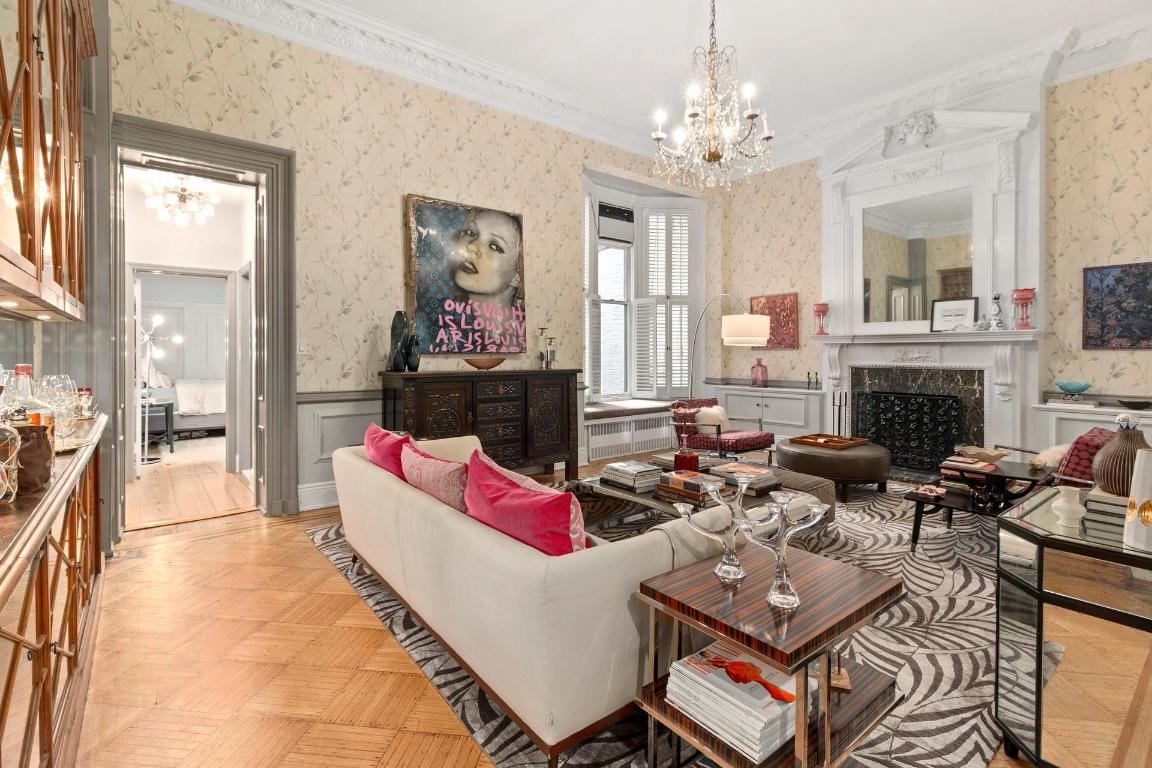 Living room with a white sofa, pink cushions, patterned rug, ornate fireplace, and chandelier.