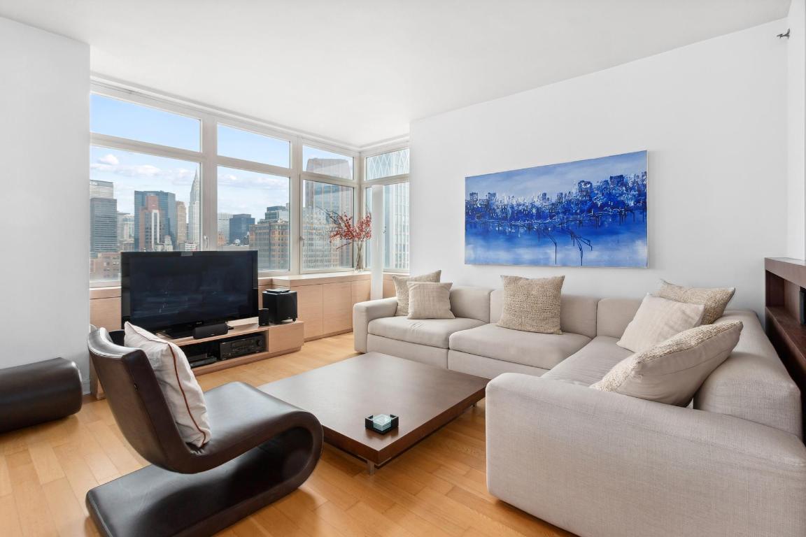 Living room with a large sectional sofa and city skyline views through floor-to-ceiling windows.