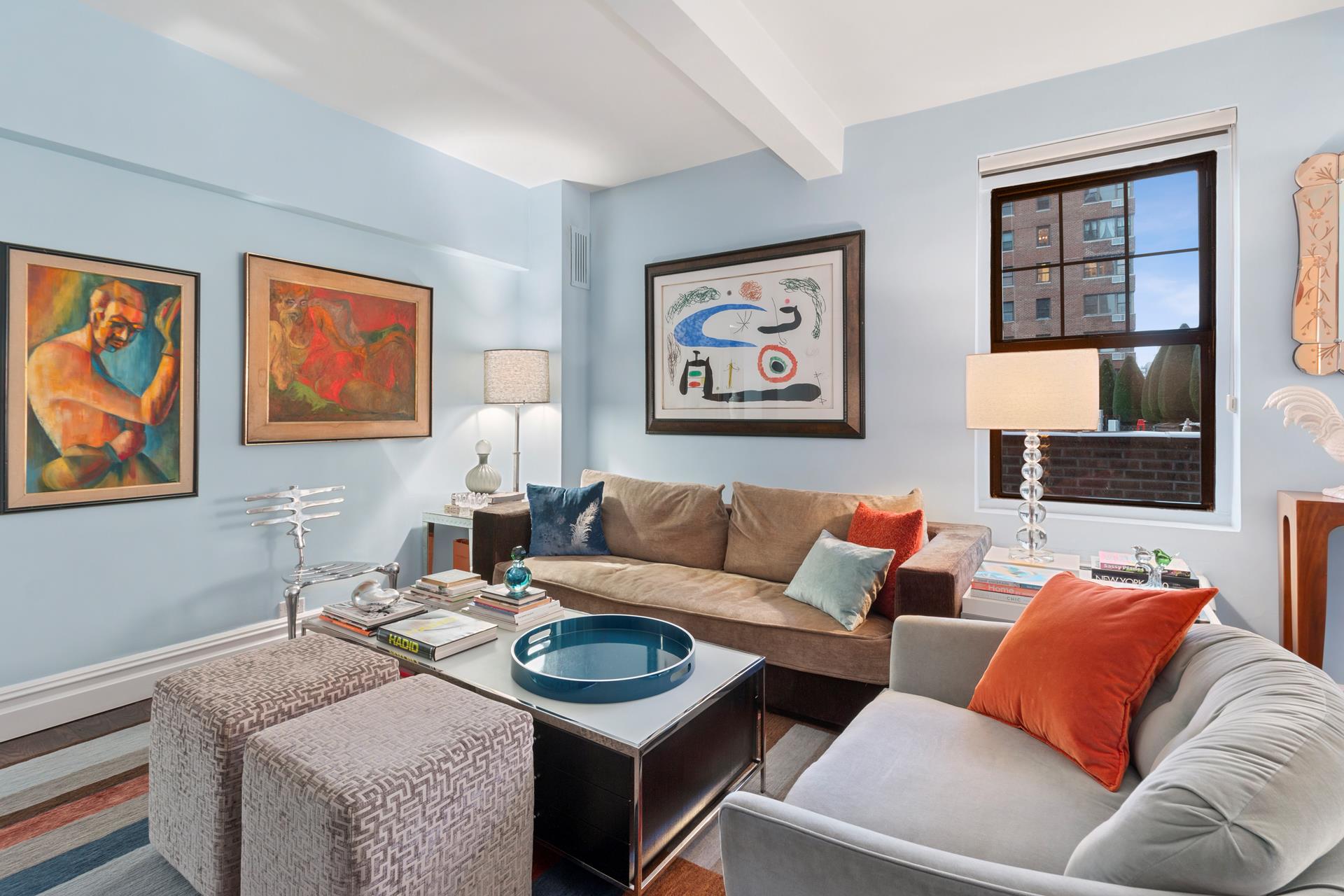 Living room with pale blue walls, framed artwork, and sofas arranged around a glass-topped coffee table.
