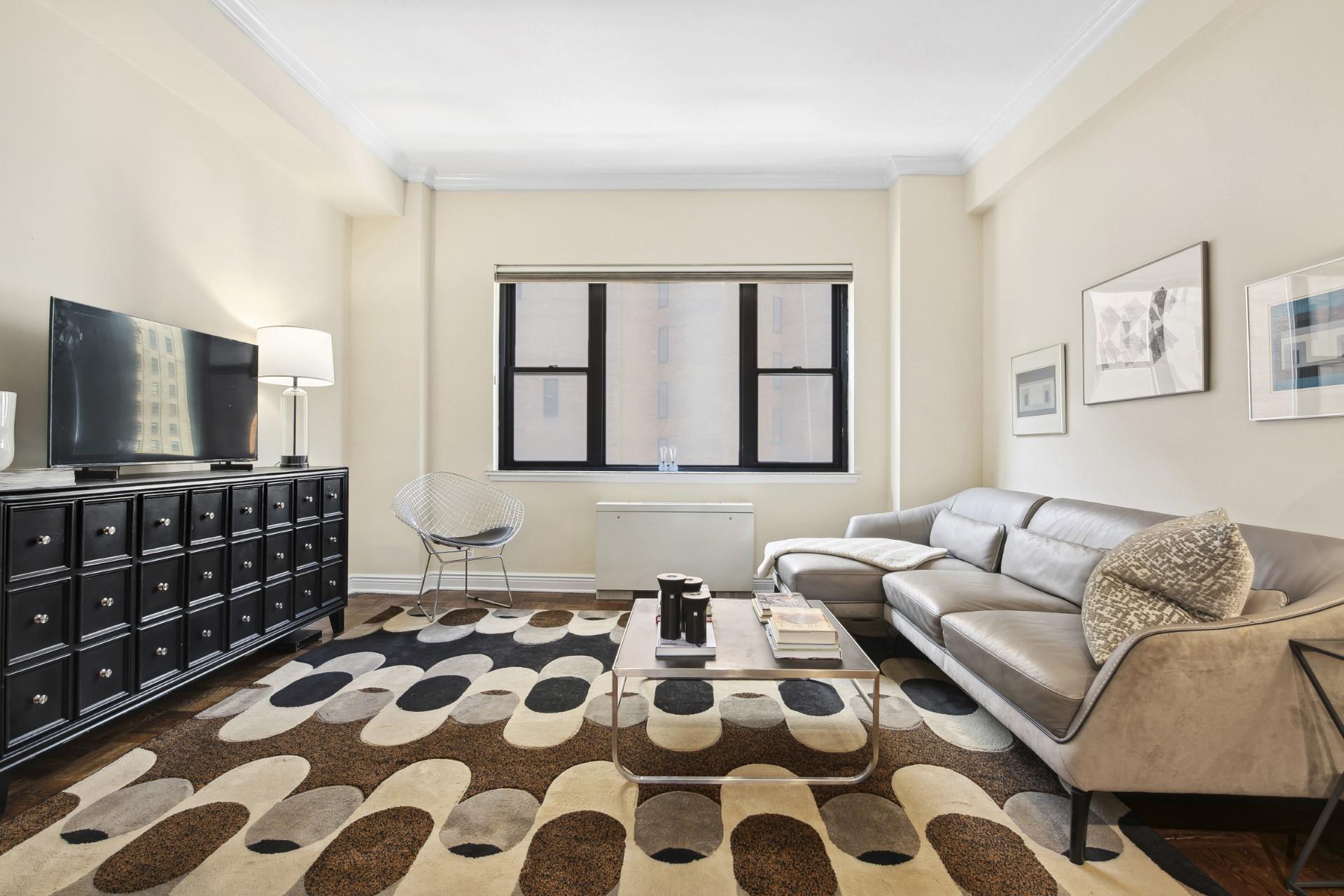 Living room with a gray sectional sofa, geometric rug, and black media cabinet beneath a television.