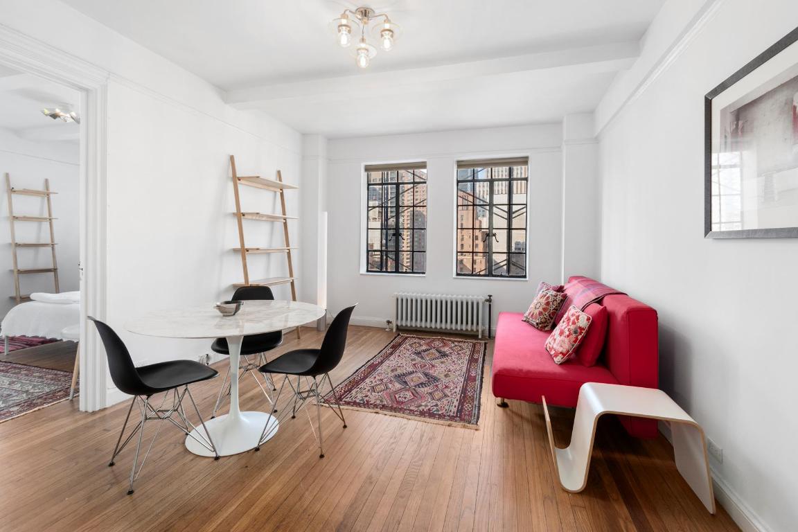 Living and dining area with a red sofa, marble table, and city buildings visible through the windows.