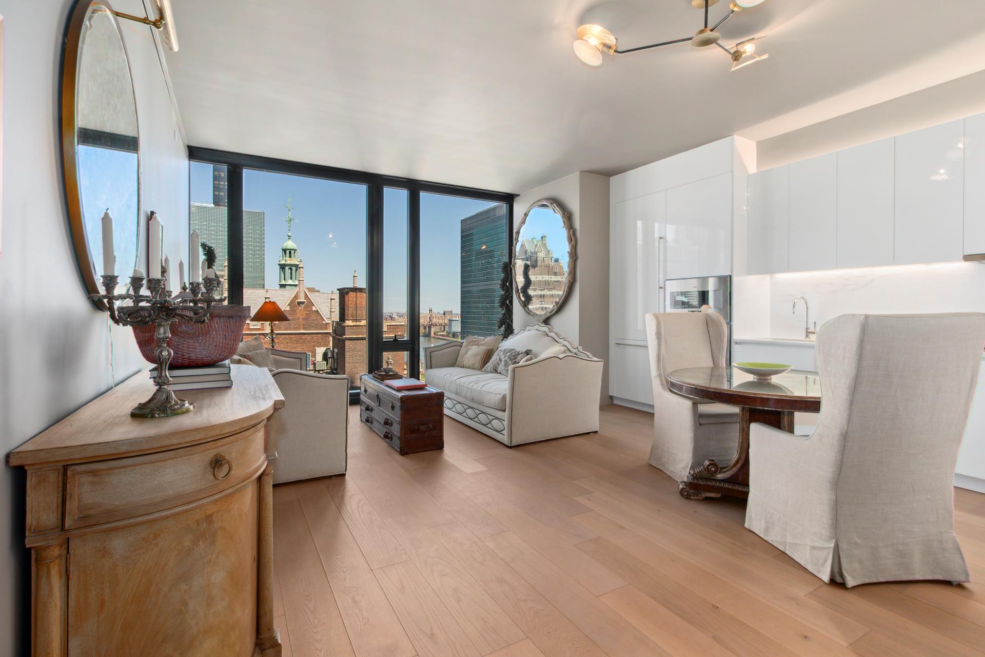 Open-plan living and dining area with floor-to-ceiling windows overlooking city buildings, a bridge, and water.