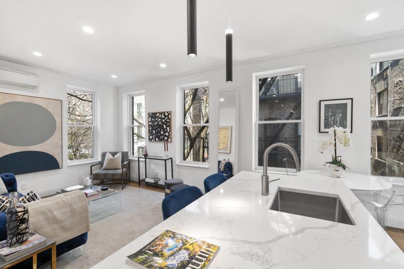 Open-plan kitchen with a marble island, integrated sink, and tall windows overlooking neighboring buildings.