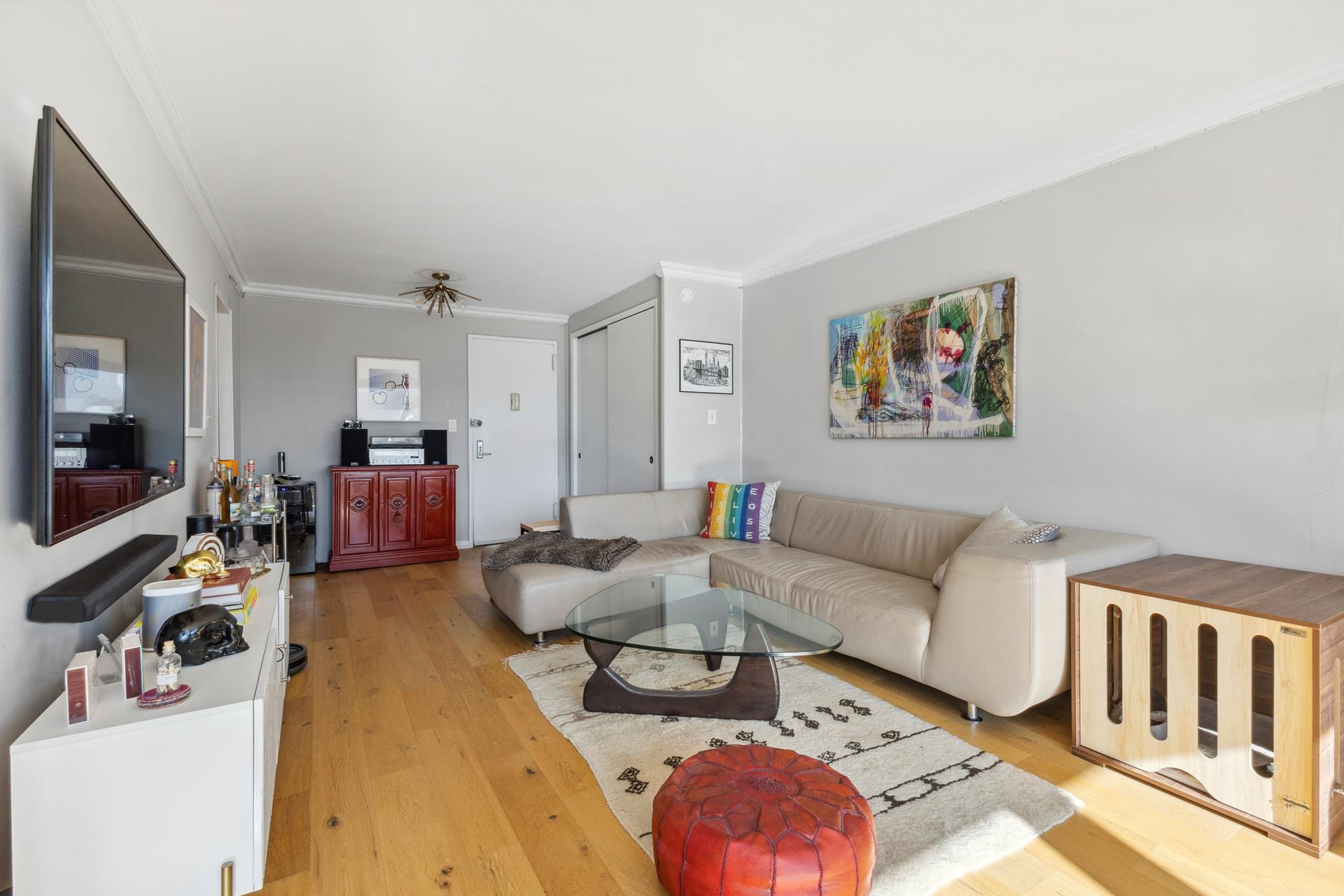 Living room with a beige sectional, glass coffee table, and colorful abstract wall art.