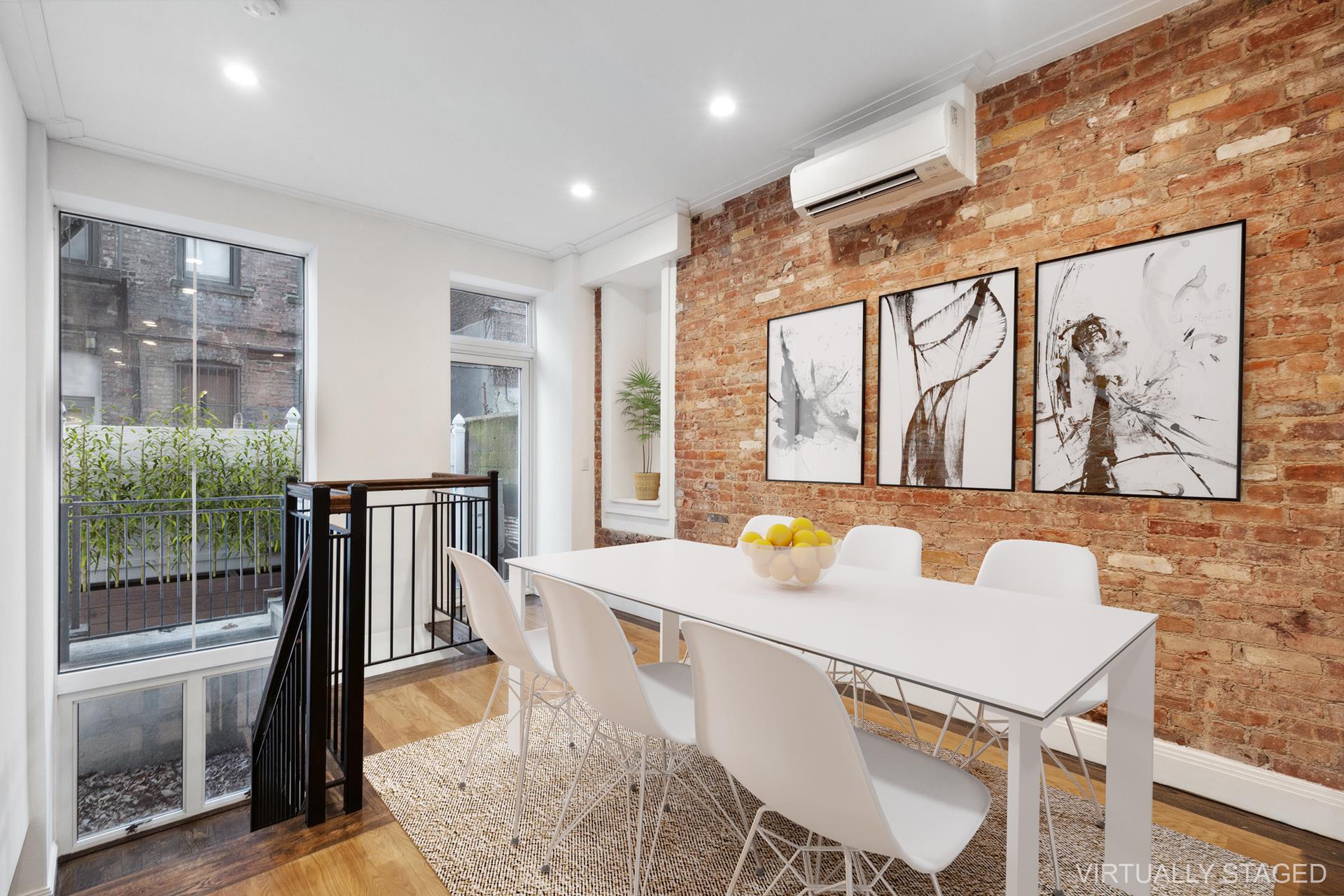 Dining area with an exposed brick wall, white table, abstract art, and tall windows.
