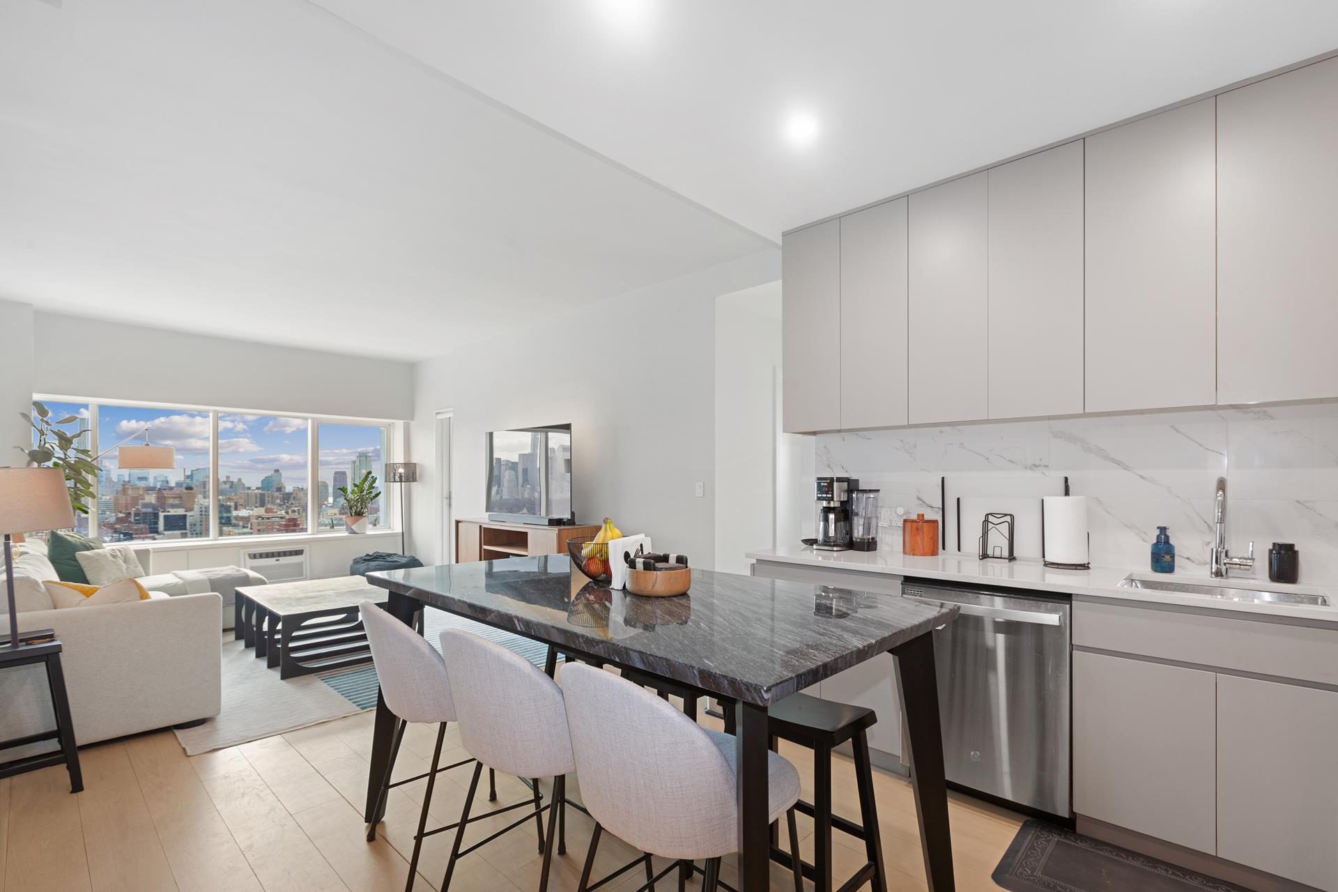 Open-plan kitchen and living area with a dark stone island and city skyline views through wide windows.