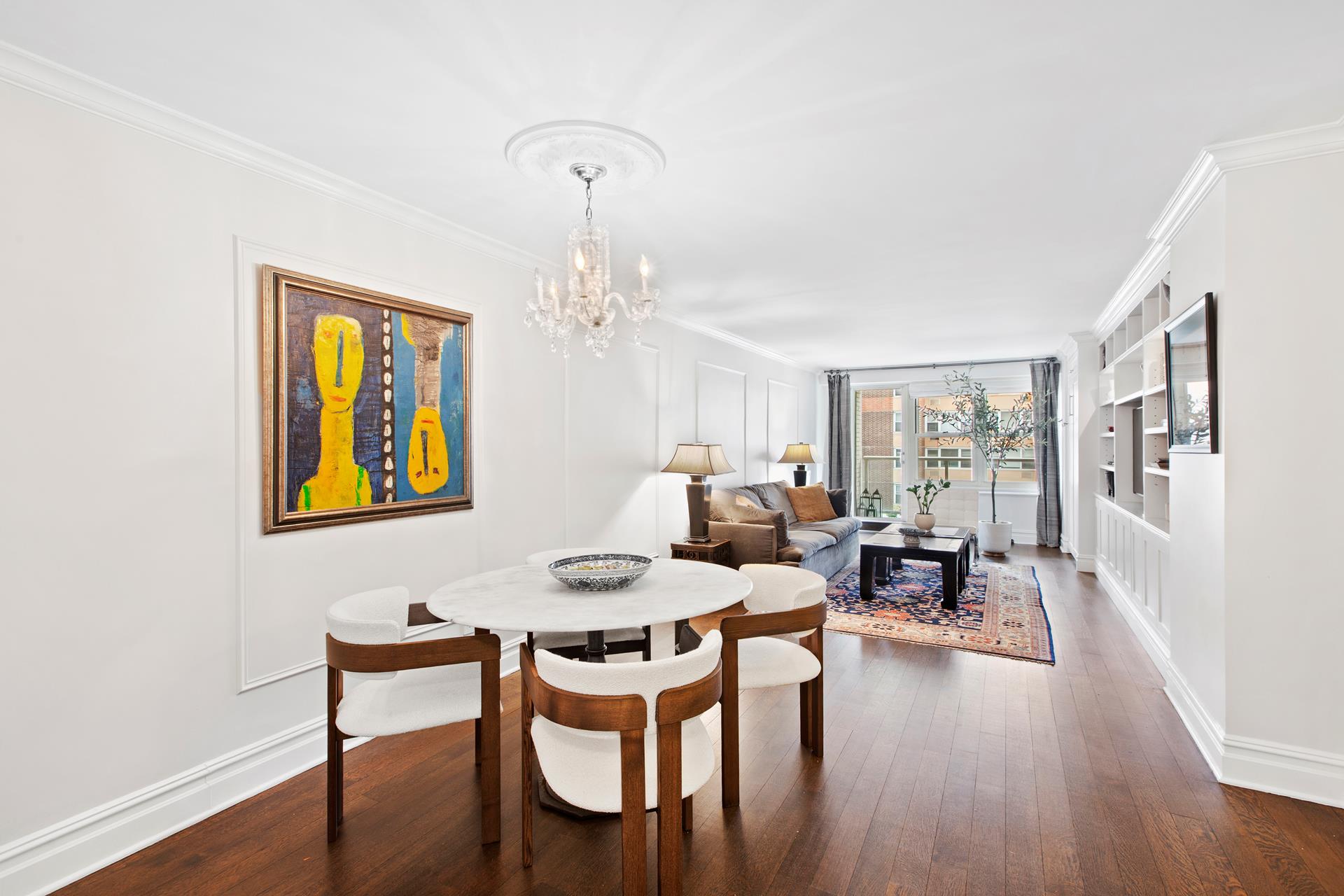 Furnished living and dining room with dark hardwood floors, white built-ins, and colorful wall art.