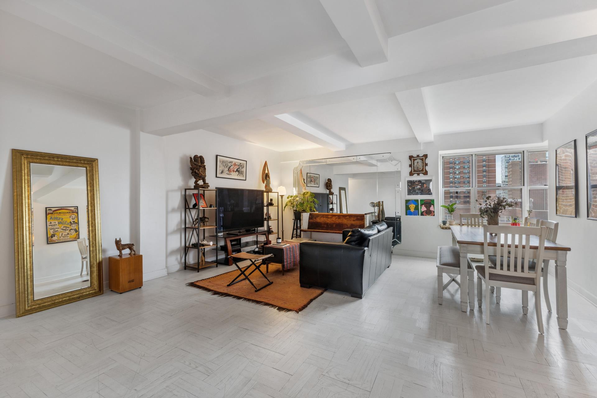 Open-plan living and dining room with white tile floors, black leather sofa, and large city-facing windows.
