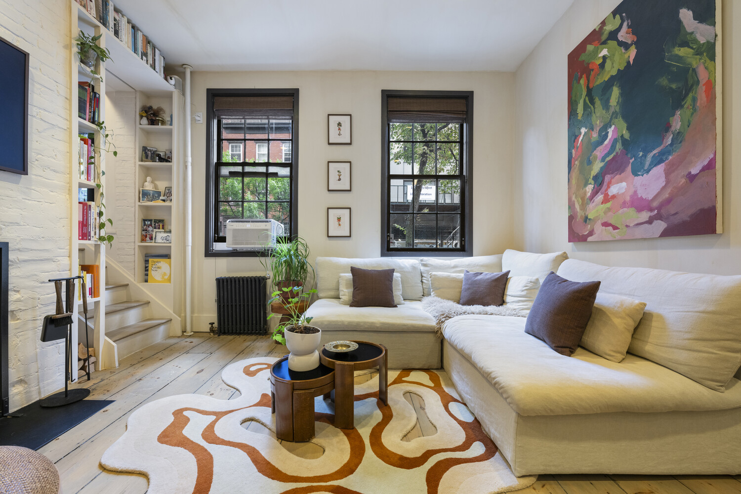Living room with a white sectional, colorful abstract painting, and built-in bookshelves beside a staircase.