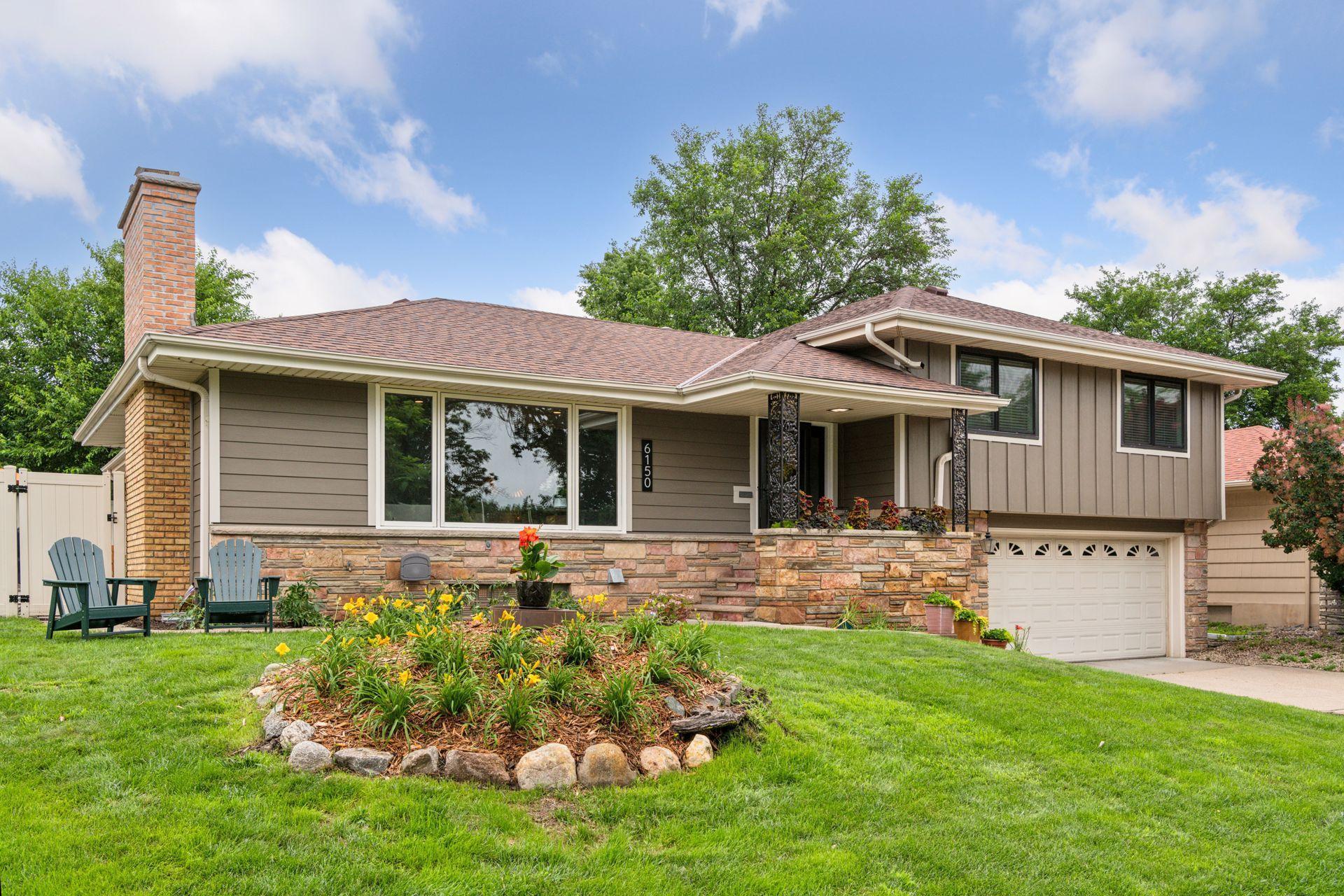 Two-story taupe home with stone accents, brick chimney, landscaped garden, and attached garage.