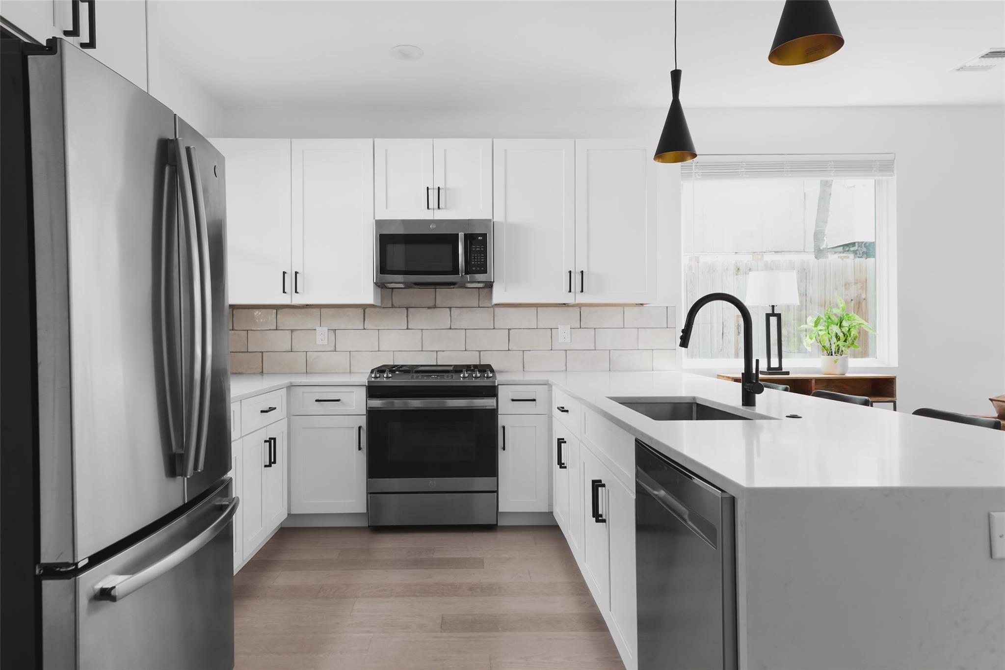 Modern white kitchen with stainless appliances, a large island, and black pendant lights.
