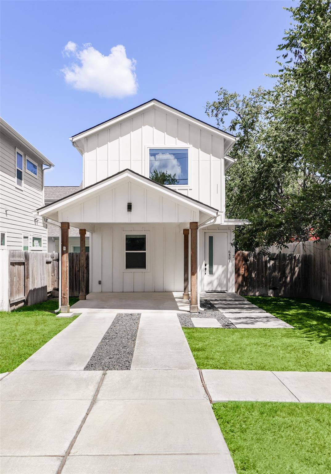 White two-story home with a covered carport, wooden fence, and concrete walkway.