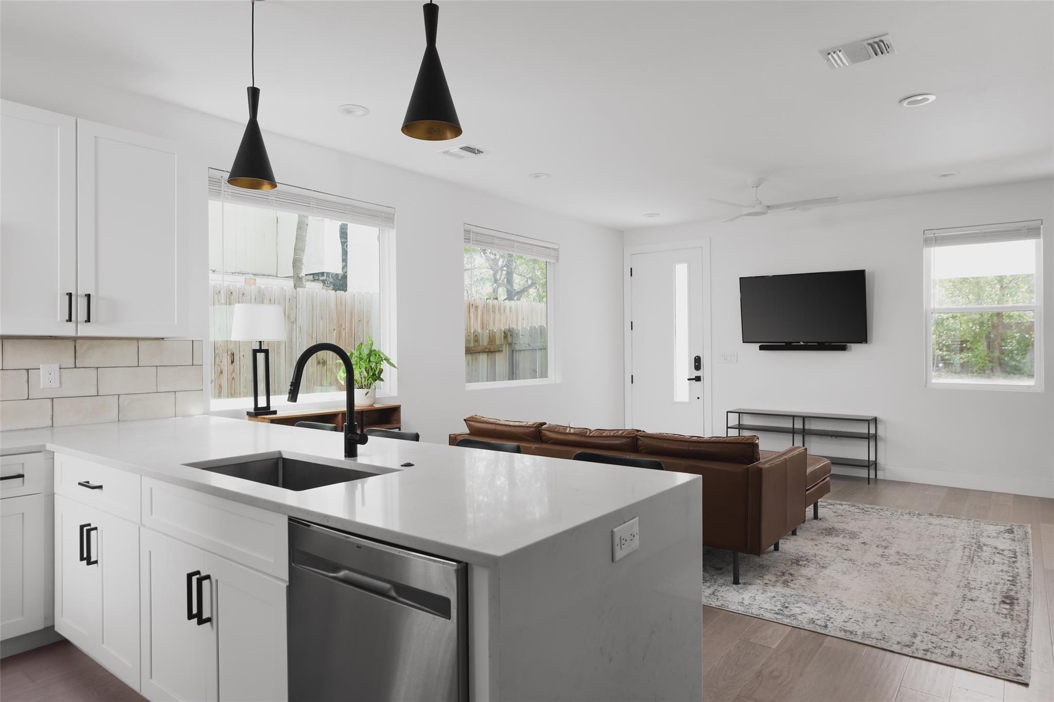 Open-plan kitchen and living room with a white island, brown leather sofa, and wall-mounted television.