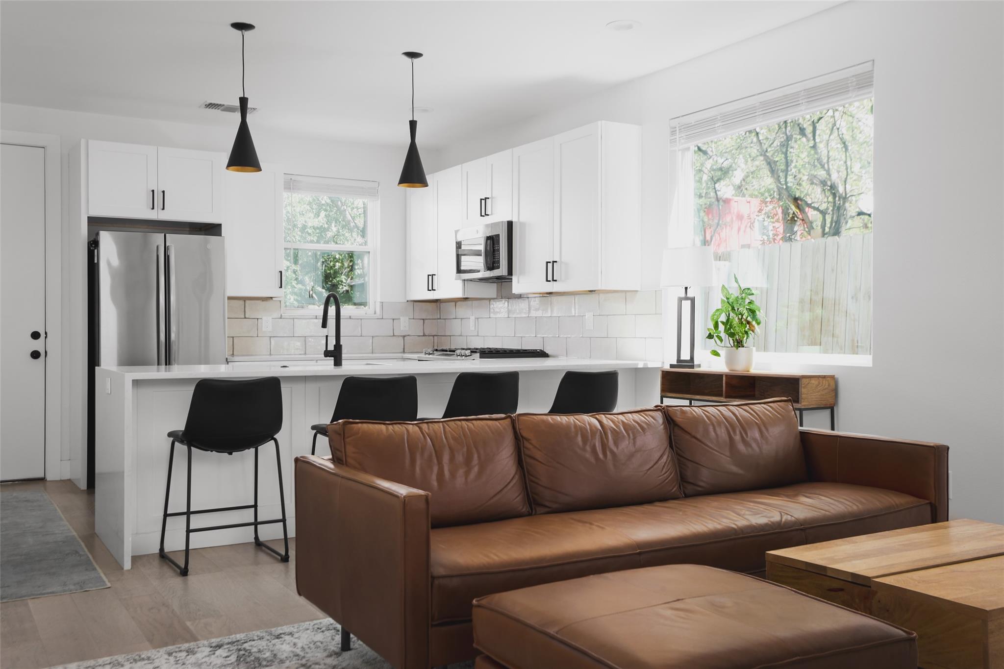 Open-plan kitchen and living area with white cabinets, black island stools, and a brown leather sectional.
