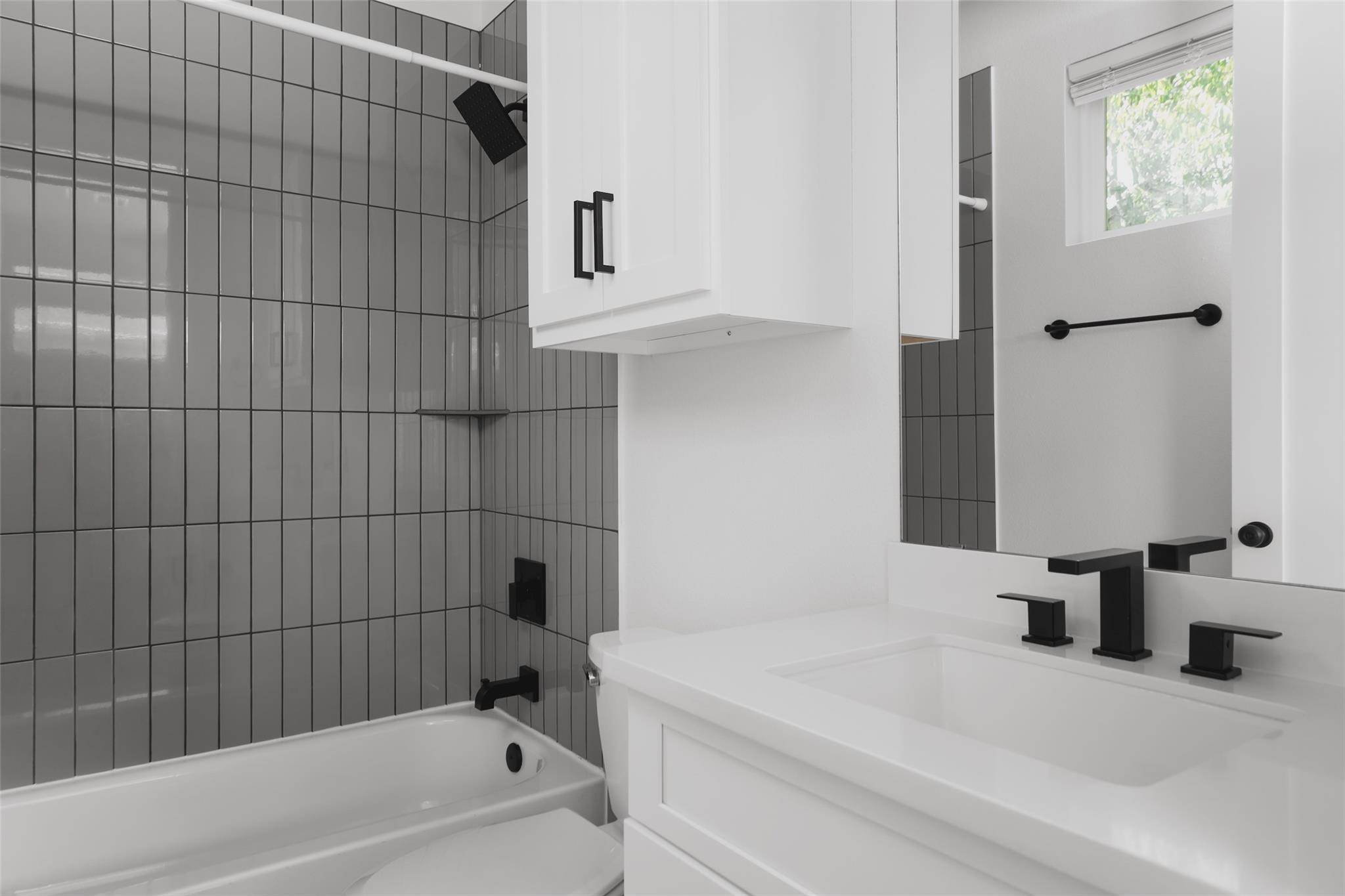 Bathroom with a white tub, glossy gray tile, and black fixtures beside a white vanity.