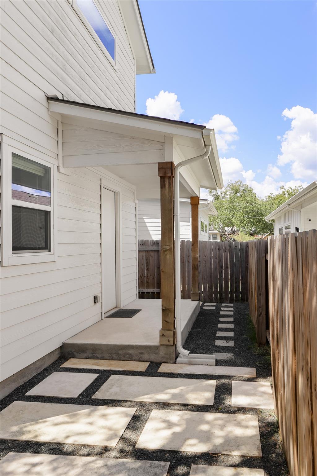 White-sided home with a covered patio and concrete pavers set in gravel along a fenced walkway.