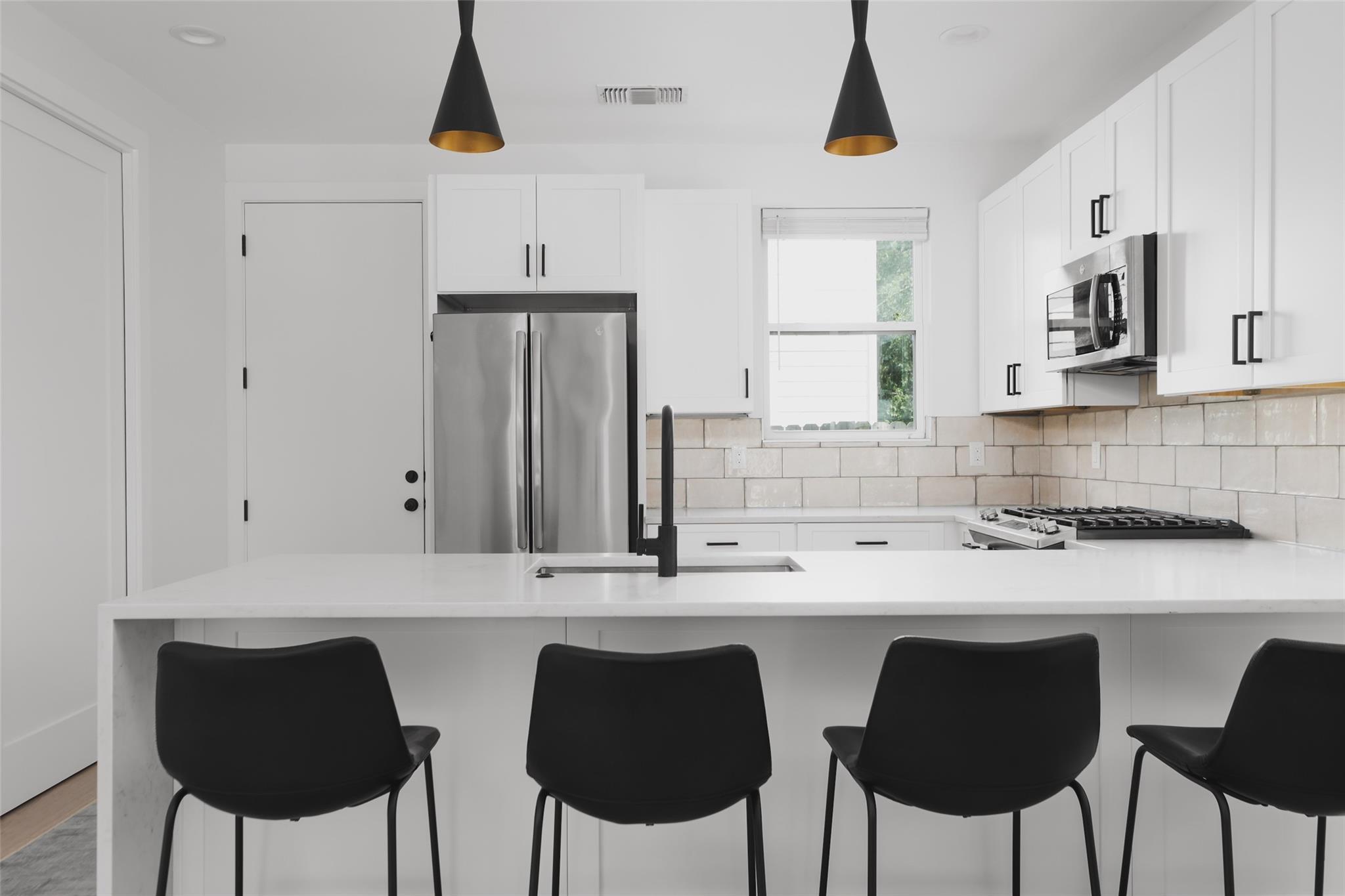 Modern white kitchen with stainless appliances, a large island, and four black bar stools.