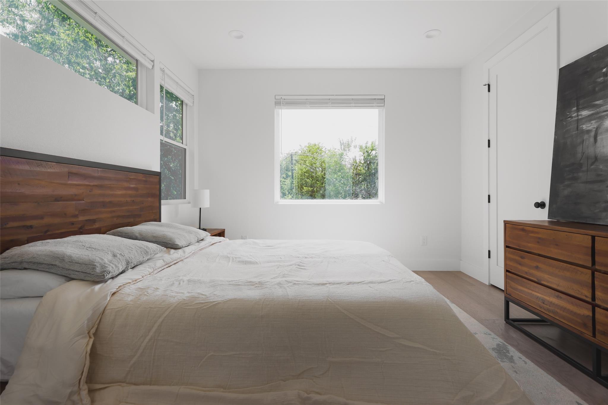 Bright bedroom with a large bed, wood plank headboard, and windows overlooking leafy trees.