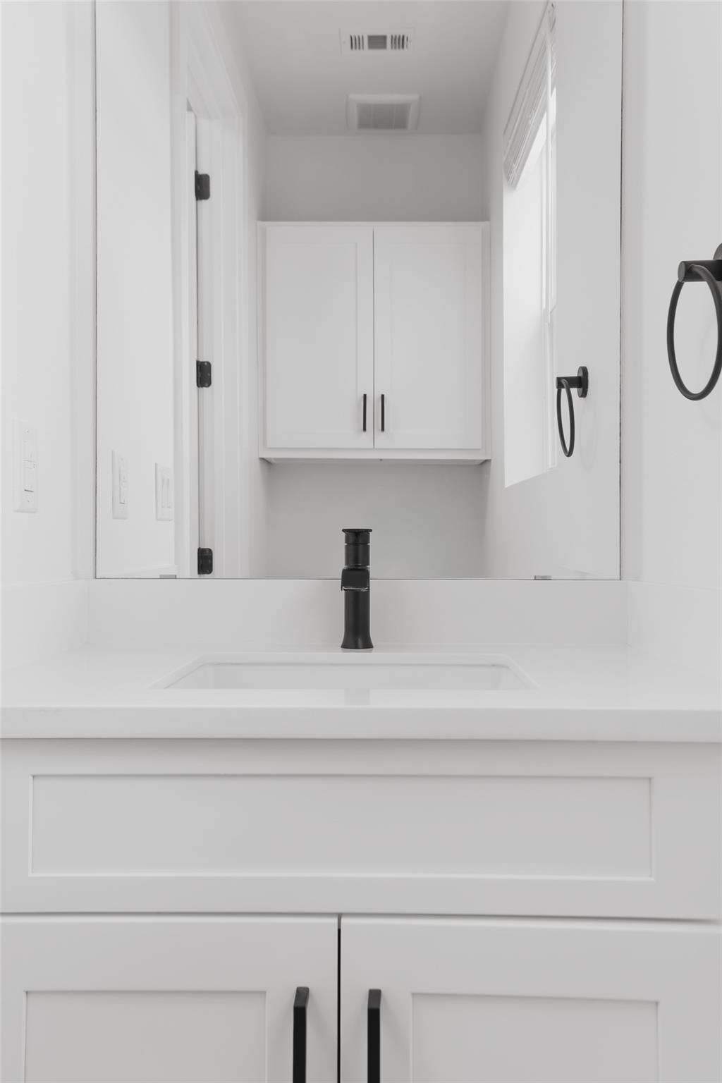 Bathroom vanity with a white sink, mirrored cabinet reflection, and matte black faucet and hardware.