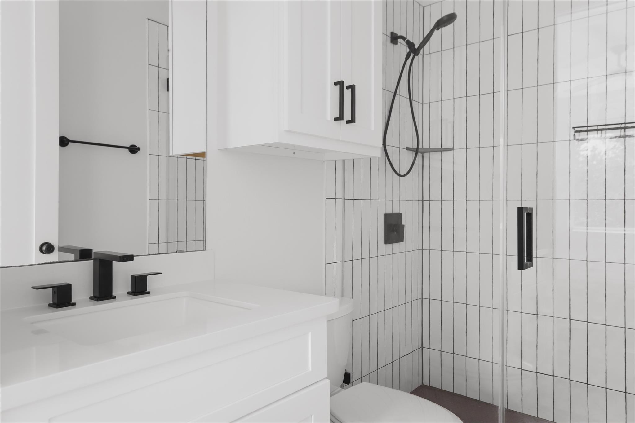 Modern bathroom with a white vanity and black fixtures beside a tiled glass shower.