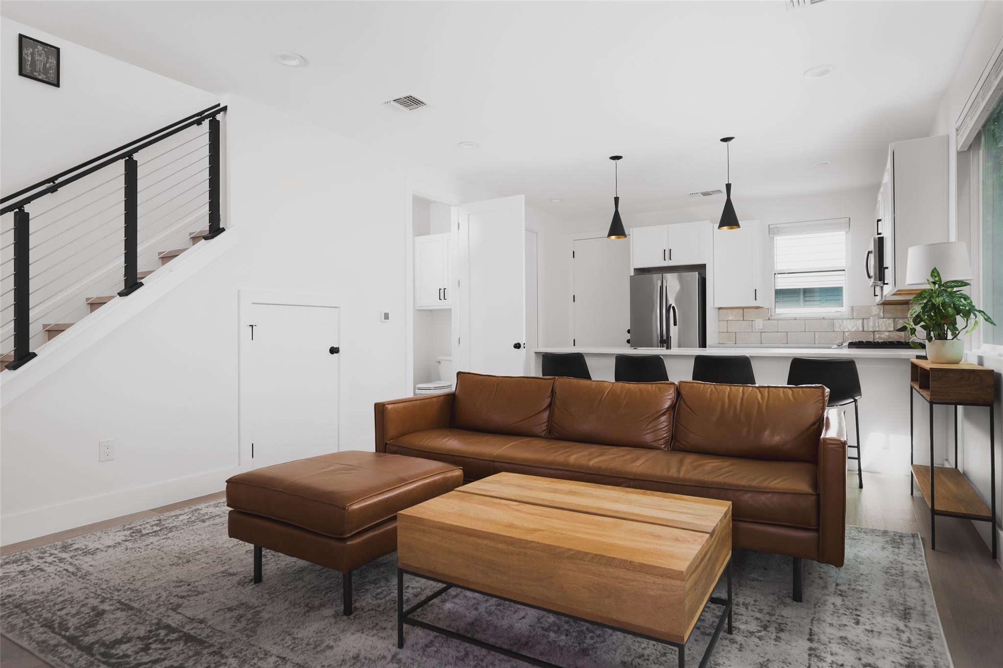Open-plan living room with a brown leather sofa, wooden coffee table, and kitchen beyond.