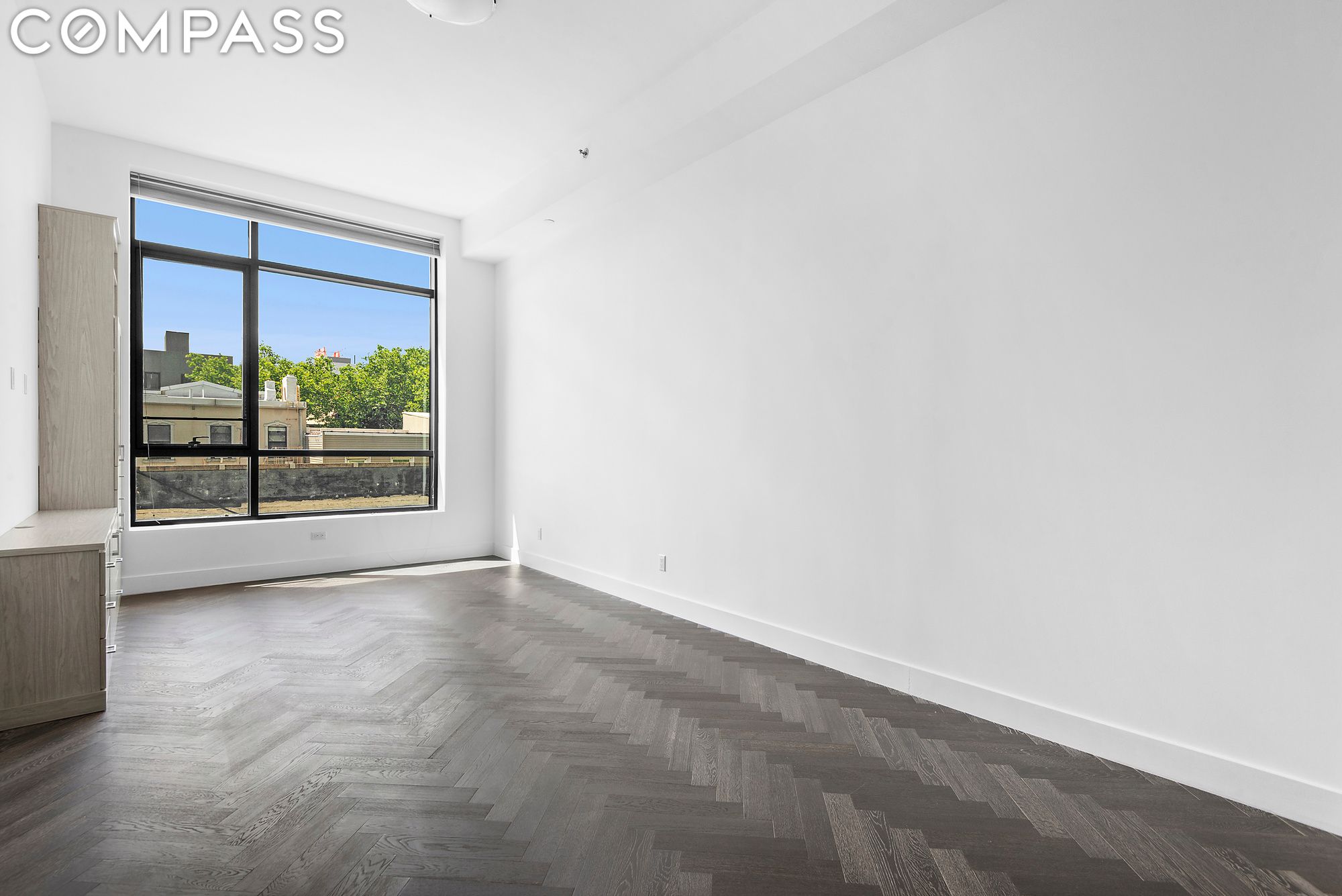 Bright vacant room with herringbone floors, built-in cabinetry, and a large black-framed window.