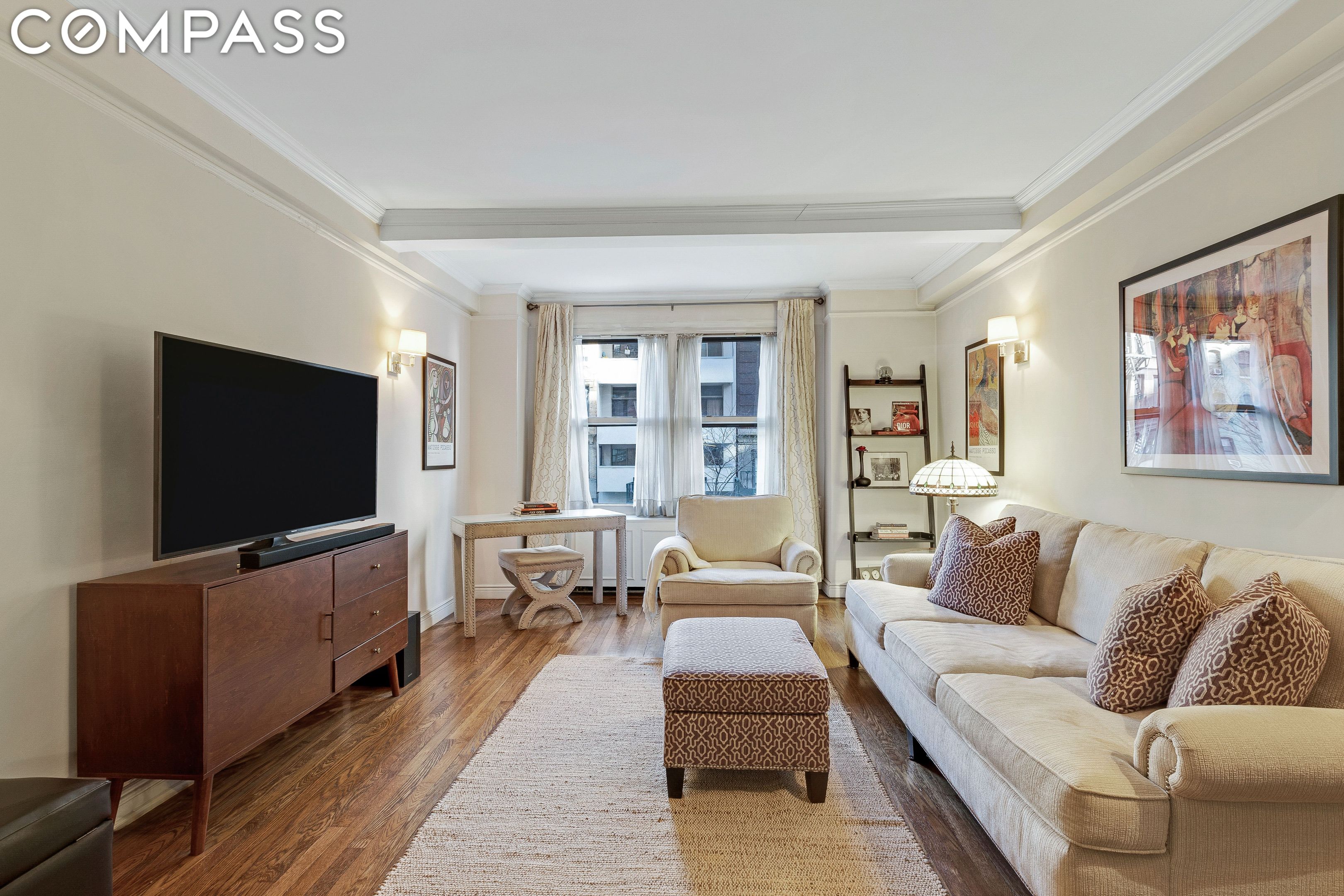 Furnished living room with a cream sofa, hardwood floors, and large windows.