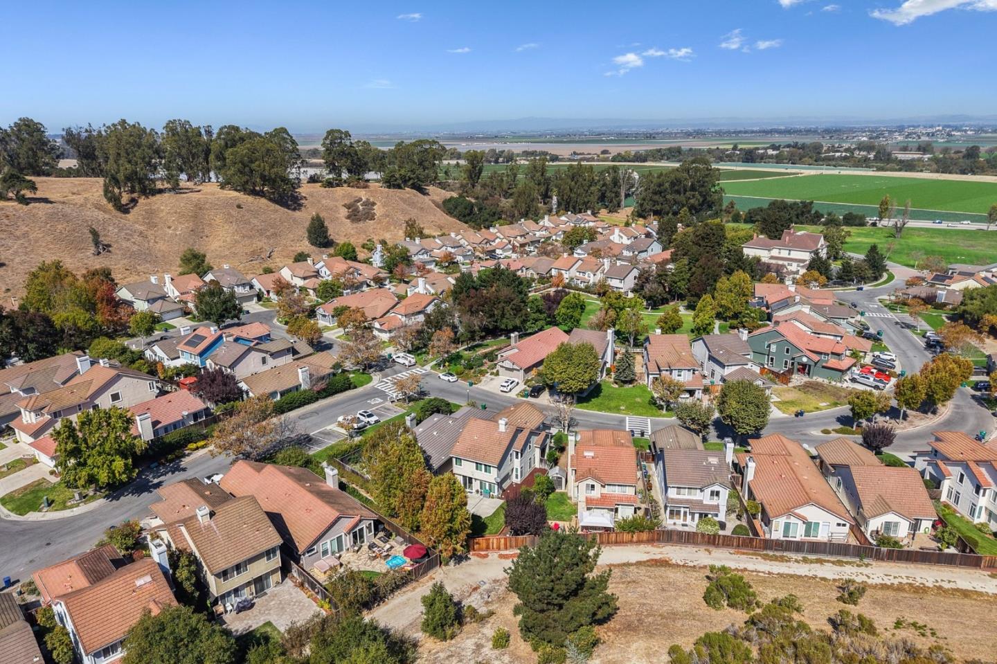 Aerial view of a residential neighborhood bordered by dry hills and green agricultural fields.