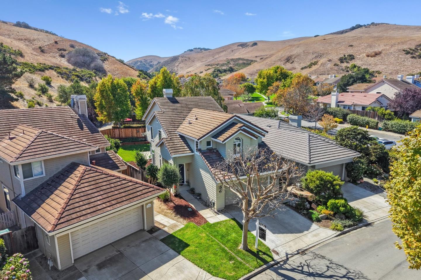 Aerial view of a two-story home with a tile roof and front lawn, backed by rolling hills.