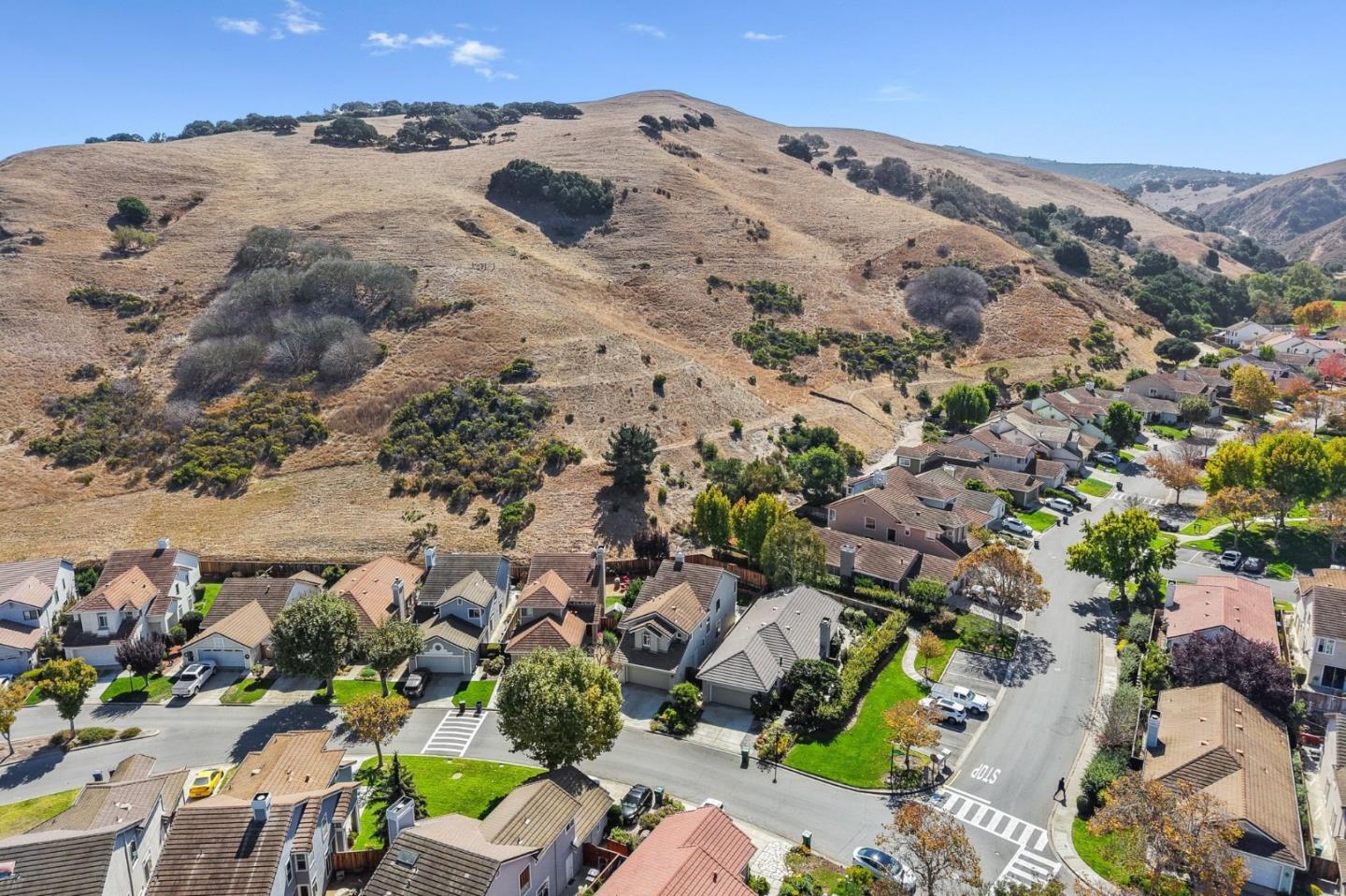 Aerial view of homes along residential streets below dry, rolling hills.