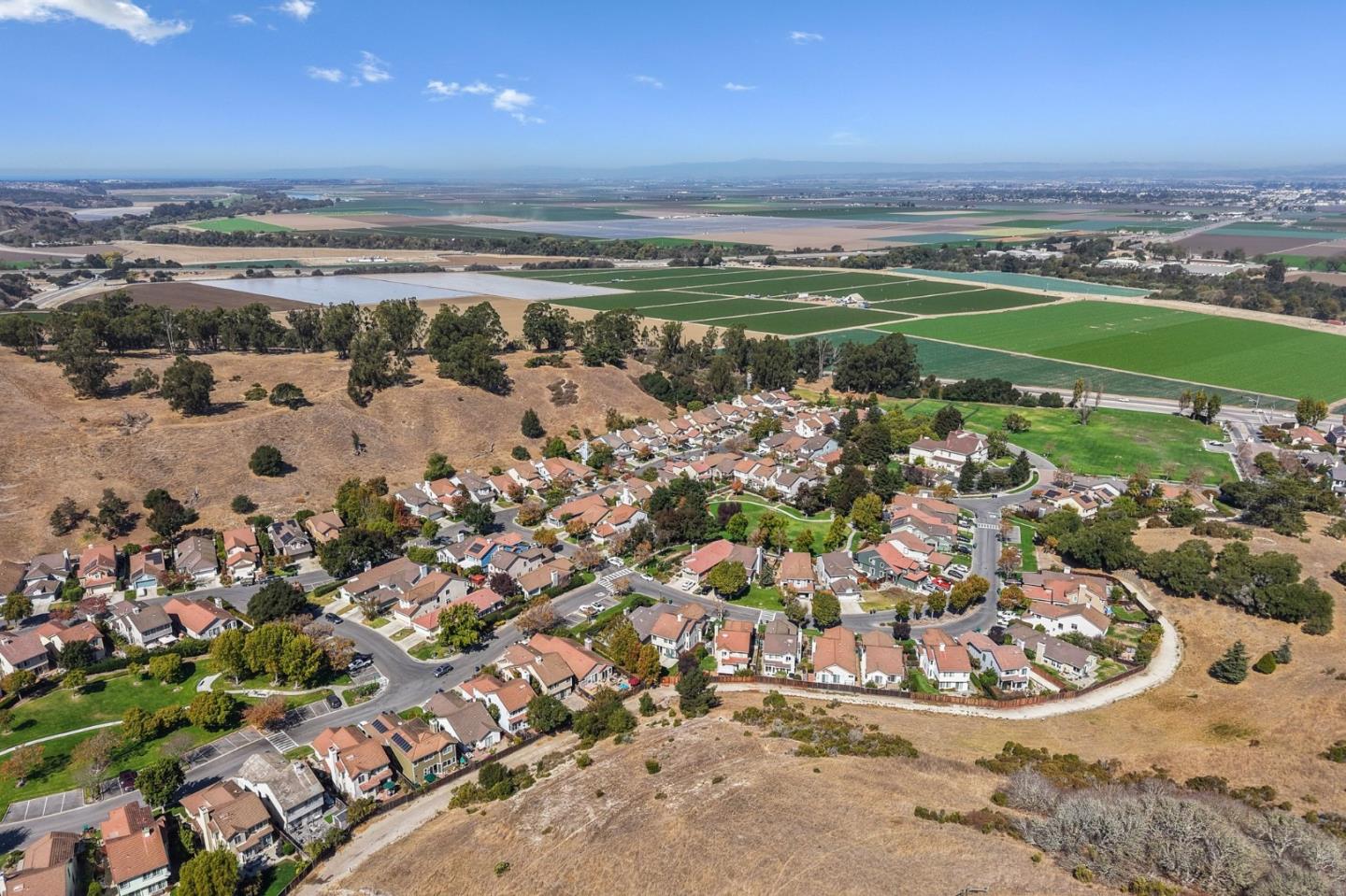 Aerial view of a neighborhood beside agricultural fields, with distant hills beyond.