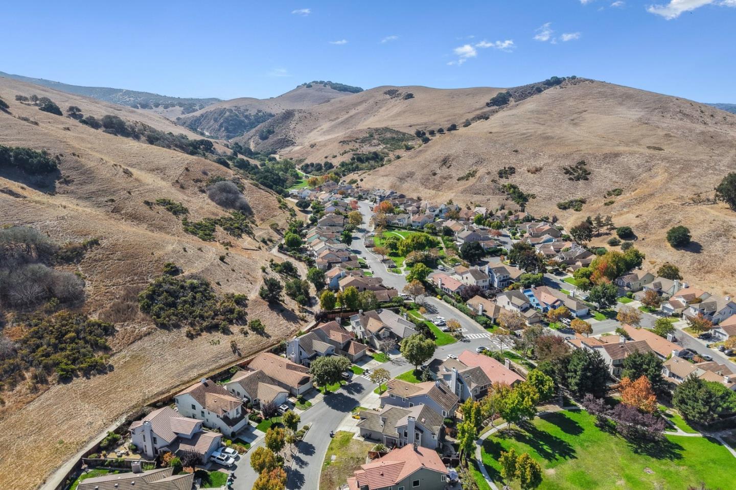 Aerial view of a neighborhood nestled among dry rolling hills, with winding streets and green lawns.