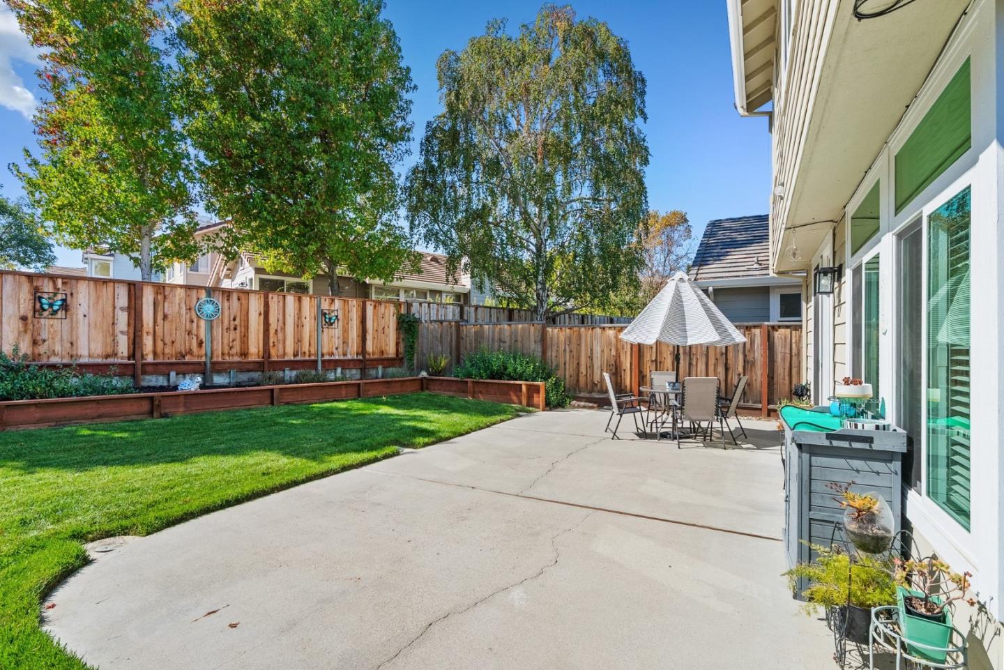 Backyard patio with outdoor dining furniture, a green lawn, raised garden beds, and a wooden privacy fence.