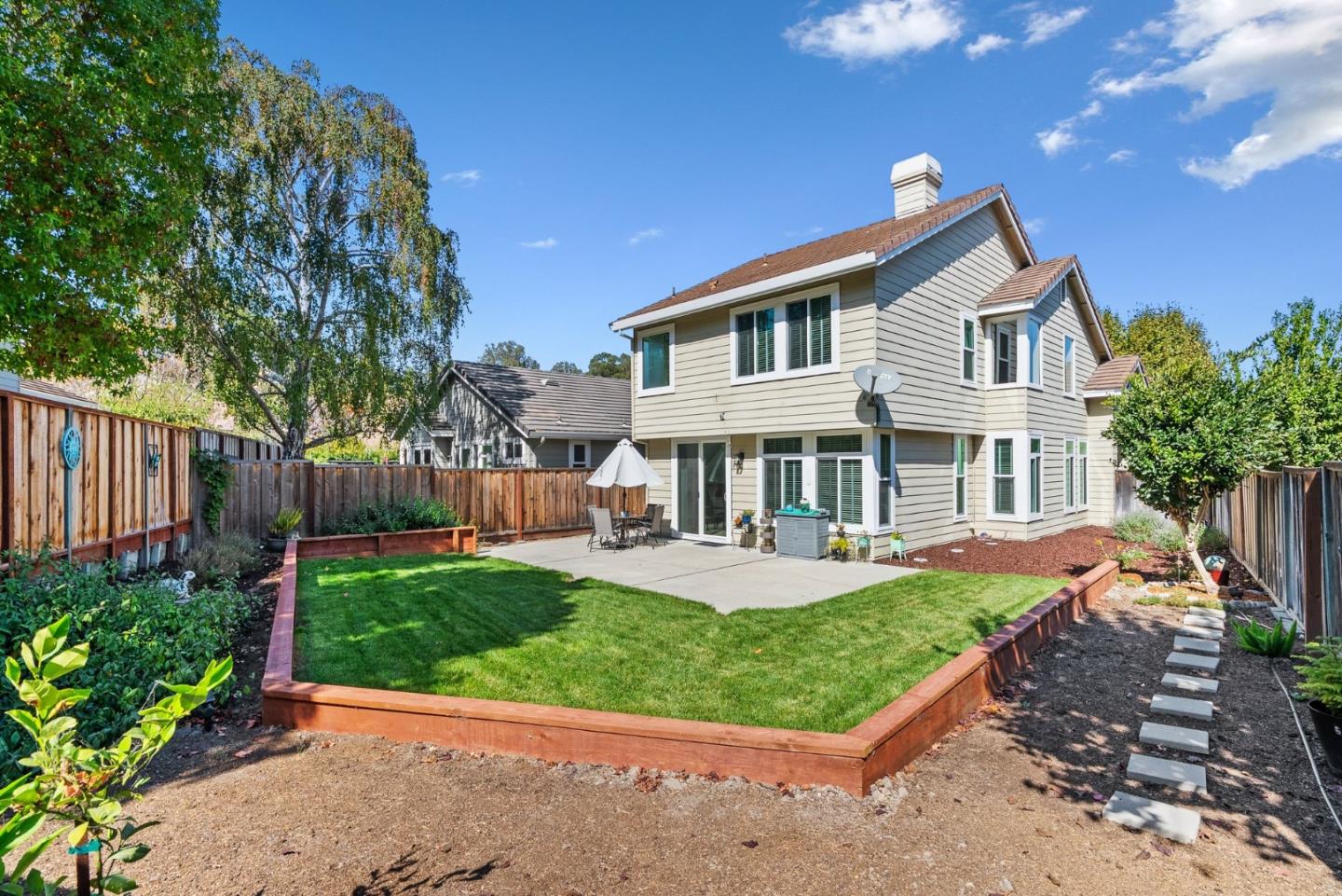 Home’s rear exterior overlooking a raised lawn, patio, and landscaped backyard.