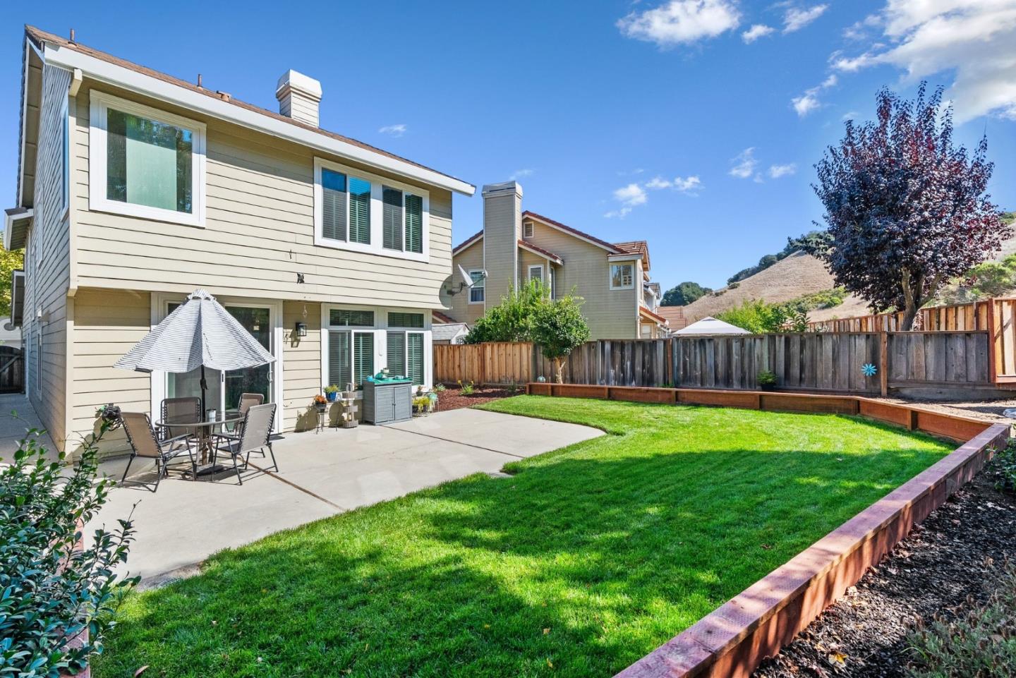 Two-story home with a concrete patio and outdoor dining set beside a fenced lawn.