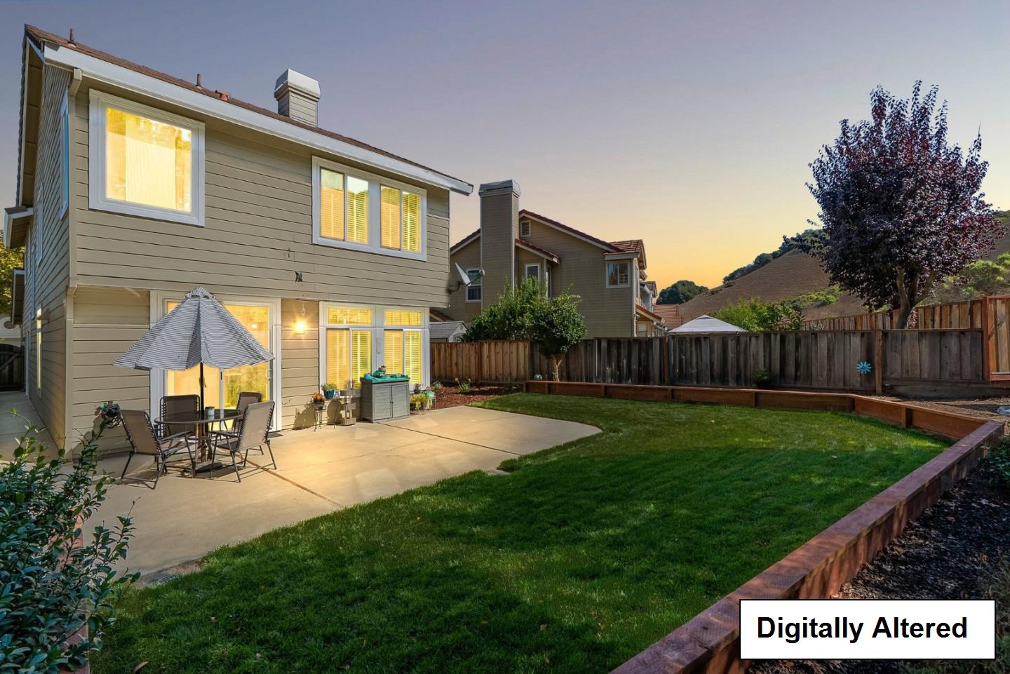 Two-story home’s backyard with a lawn, concrete patio, and outdoor dining set at sunset.