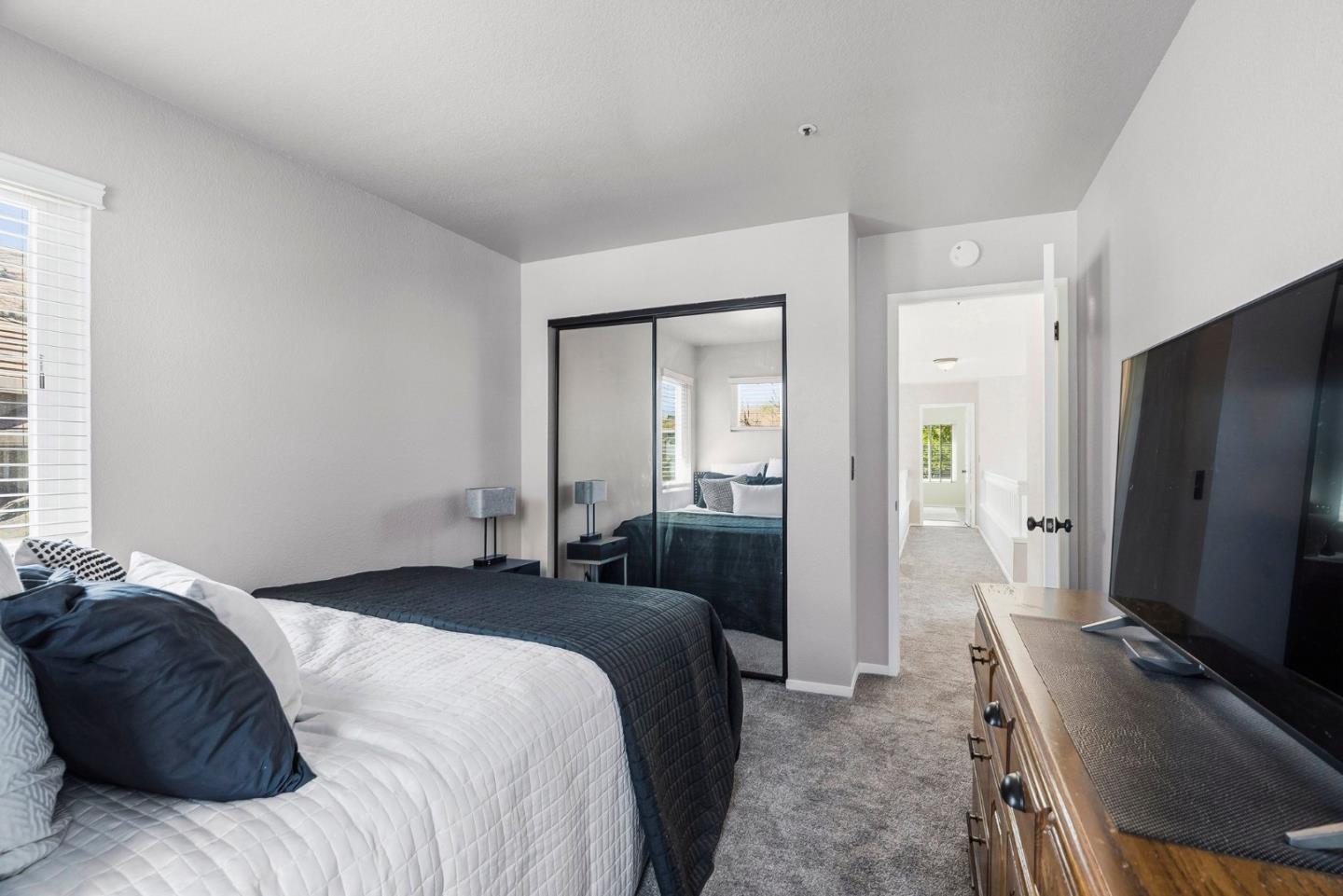 Furnished bedroom with mirrored closet doors, dark blue bedding, and a wooden dresser with television.